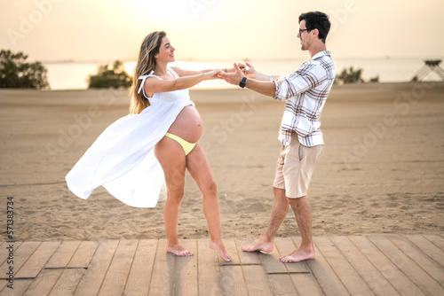 Beautiful young pregnant couple holding hands and dancing on the beach.