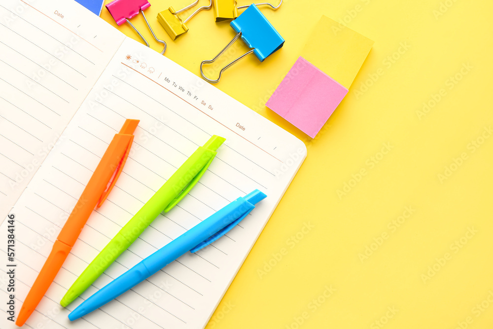 Notebook, pens, sticky notes and paper clips on yellow background, closeup Notebook, pens, sticky notes and paper clips on yellow background, closeup