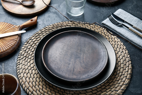 Beautiful table setting with wooden plates and tree branch on dark background, closeup