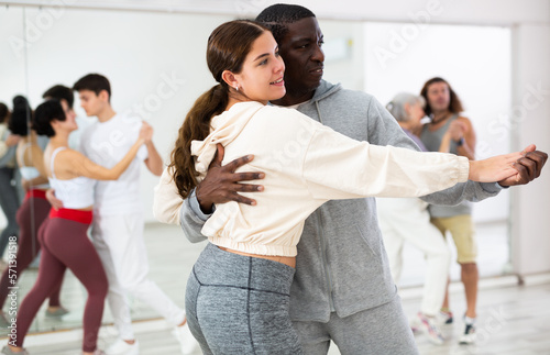 Positive couple of dancers, engaged in a dance studio for adults, learns a slow foxtrot in lesson