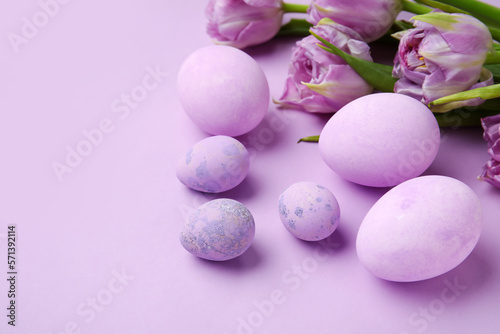 Easter eggs and beautiful tulip flowers on lilac background, closeup
