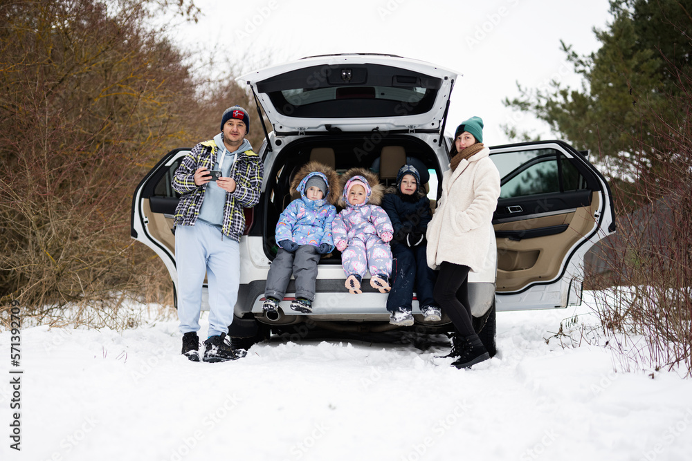 Family with kids sit on car suv with open trunk stand in winter forest.