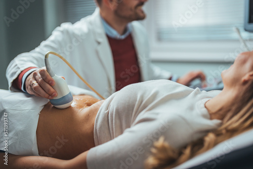 Selective focus on ultrasound scanner device in the hand of a professional doctor examining his patient doing abdominal ultrasound scanning sonogram sonography sonographer early pregnancy photo