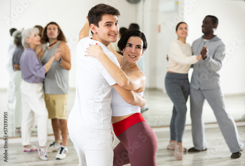 Young smiling guy learning to dance waltz paired with expressive positive Hispanic girl in dancing class