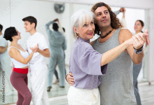 Positive adult man and smiling aged woman practicing modern paired dance movements in group dance class