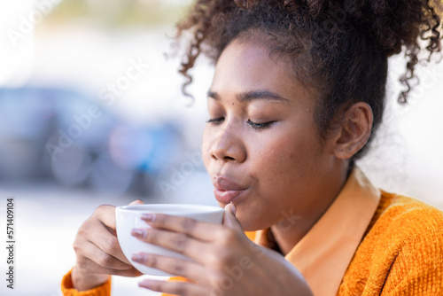Focused African American biracial woman student with afro hairstyle wear yellow cardigan, have a hot drink and sitting at outside working doing remote job on laptop, 