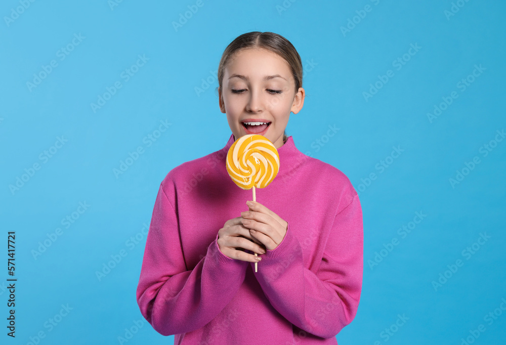 Teenage girl eating delicious lollipop on light blue background Teenage girl eating delicious lollipop on light blue background