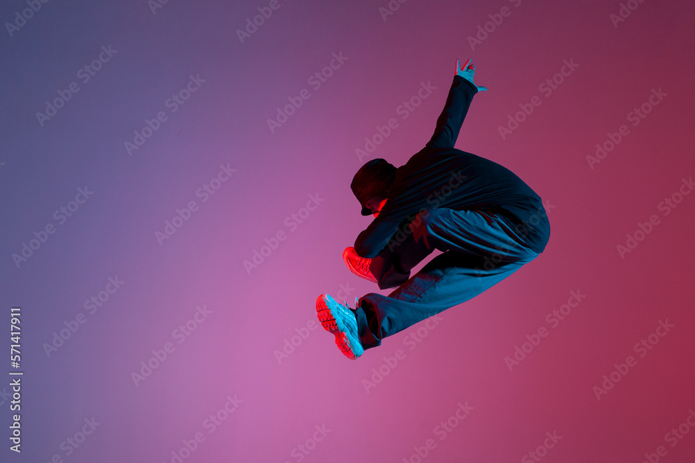 energetic guy dancer jumping in neon red blue lighting, man doing trick in flight, movement and freedom concept