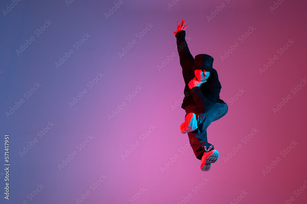 energetic guy dancer jumping in neon red blue lighting, man doing trick in flight, movement and freedom concept