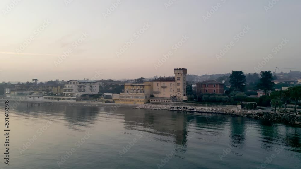 Foggy morning in town of desenzano del garda in italy, drone flies over sleepy city at sunrise with fog over lake garda, aerial view of harbor and tourist vacation village Foggy morning in town of desenzano del garda in italy, drone flies over sleepy city at sunrise with fog over lake garda, aerial view of harbor and tourist vacation village