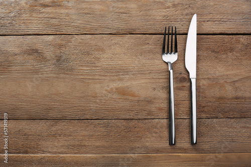 Fork and knife on wooden table, flat lay with space for text. Stylish shiny cutlery set