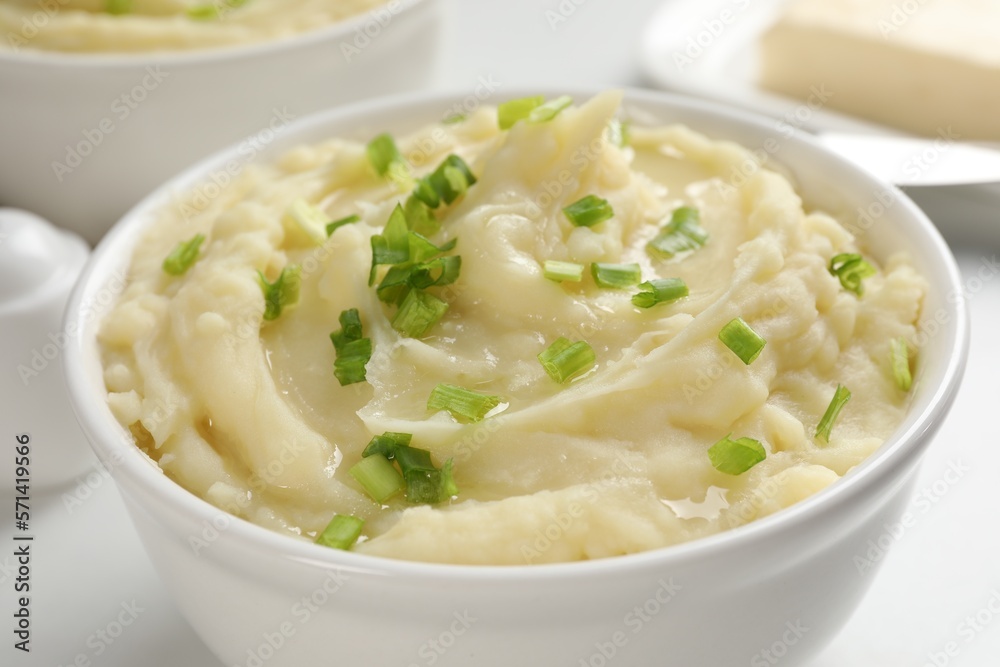 Bowl of delicious mashed potato with green onion on white table, closeup