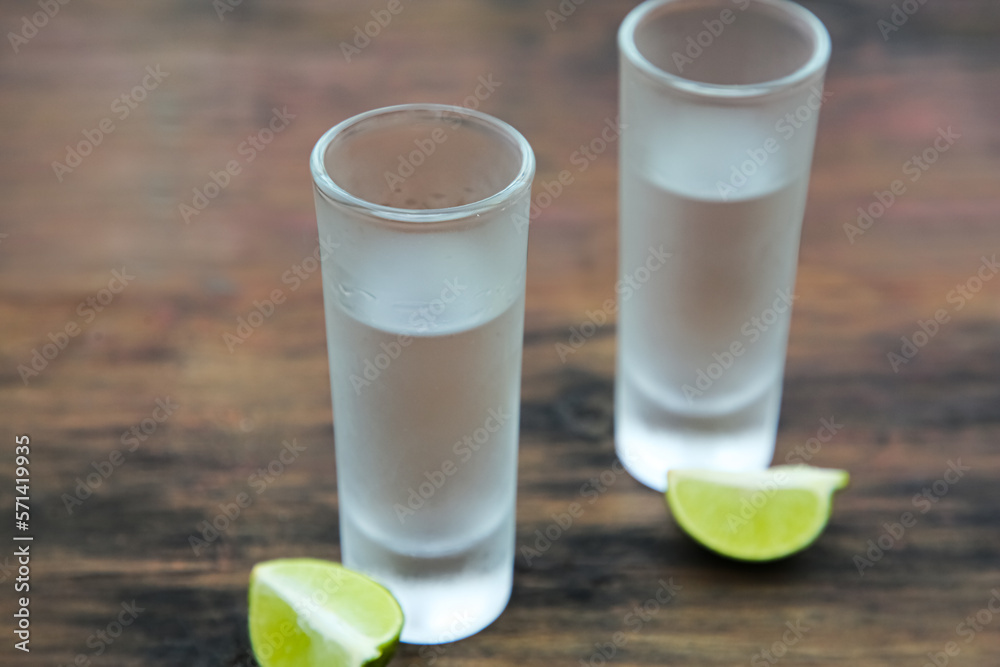 Mexican tequila shots with lime slices on wooden table, closeup. Drink made from agave Mexican tequila shots with lime slices on wooden table, closeup. Drink made from agave