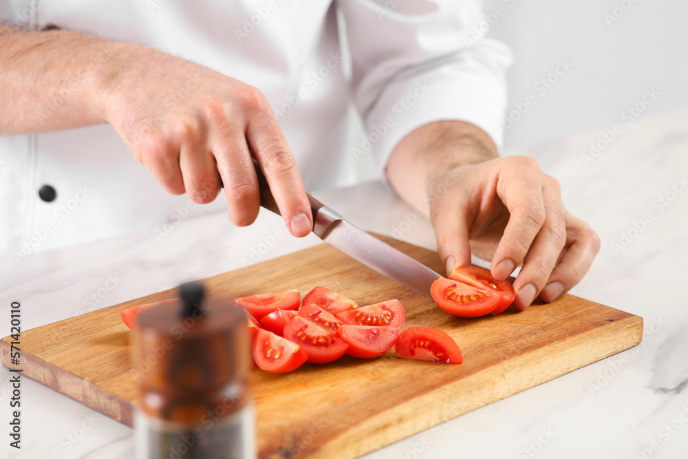 Chef cutting tomatoes at marble table in kitchen, closeup