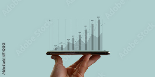 Hand holding smart phone and financial performance showing the financial growth and development of the business increases year by year. Technology makes it easy to access financial information.