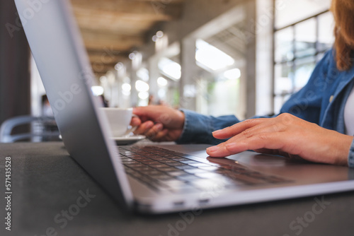 Closeup image of a young woman using and working on laptop computer while drinking coffee