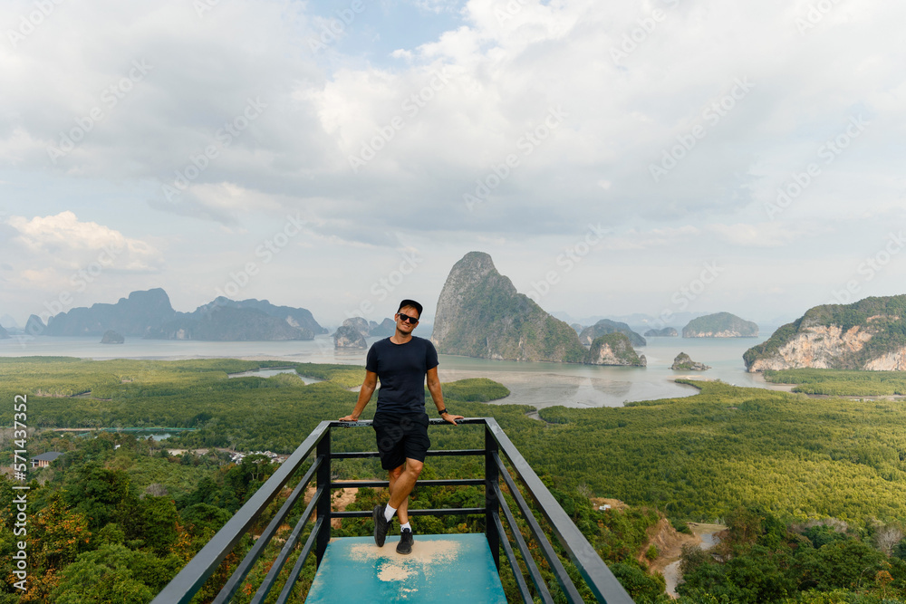 Happy traveler man enjoy Phang Nga bay view point, alone Tourist standing and relaxing at Samet Nang She, near Phuket in Southern Thailand. Southeast Asia travel, trip and summer vacation concept
