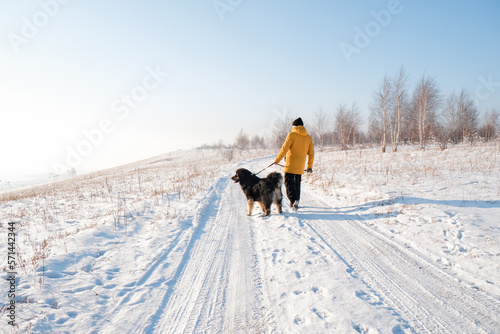 Male in yellow coat walking with his big black dog on winter background. Family winter activity with pet on sunny day outdoor. Mongolian dog breed. 