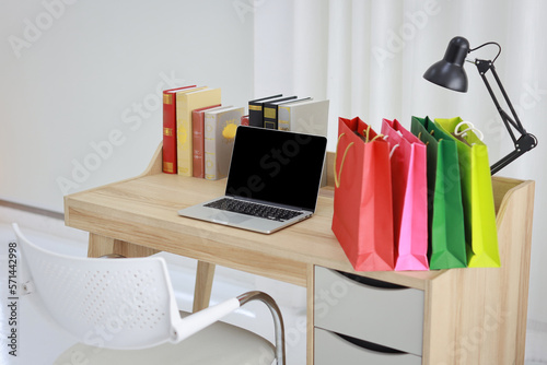 Shopping bags on wooden working table with computer black blank screen and books in room house indoor. Free space for your advertisement © feeling lucky