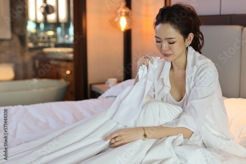 Young depressed asian woman sitting and holding handkerchief while crying on bed in hotel bedroom with low light environment. Sad girl, unhappy and loneliness concept. © feeling lucky