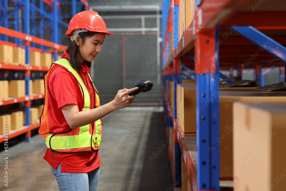 Warehouse workers woman with hardhats and reflective jackets scanning barcode on large box package for delivery to production stock and inventory in retail warehouse logistics, distribution center Warehouse workers woman with hardhats and reflective jackets scanning barcode on large box package for delivery to production stock and inventory in retail warehouse logistics, distribution center