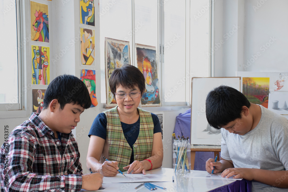 Asian middle-aged female art teacher is explaining the process of pencil drawing, sketching and shading to early teenage students in her art classroom, raising teens and adult helps kid works concept. Asian middle-aged female art teacher is explaining the process of pencil drawing, sketching and shading to early teenage students in her art classroom, raising teens and adult helps kid works concept.