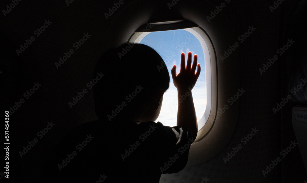Airplane window view, boy hands on the window looking out to see the clouds in the air, adventure travel concept.