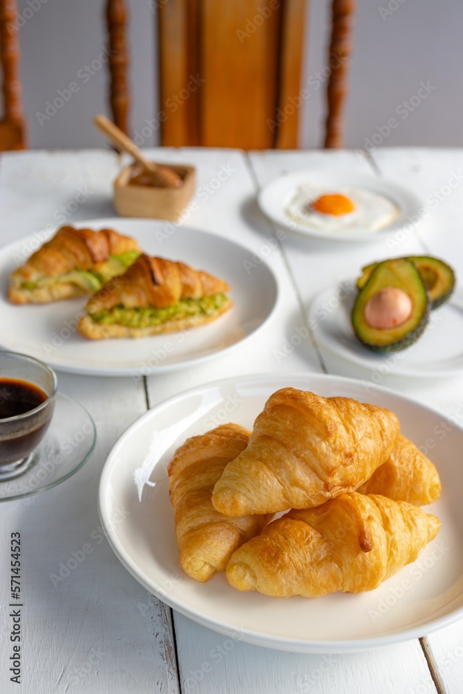Croissant sandwich with egg,avocado on white dish and honey, coffee. breakfast and healthy food concept..