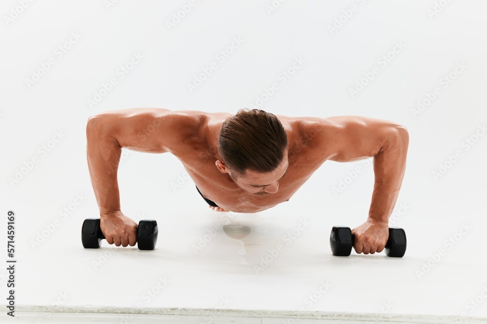 Man athletic body bodybuilder posing with dumbbells with naked torso abs full-length in the background, fitness class. Advertising, sports, active lifestyle, competition, challenge concept. Man athletic body bodybuilder posing with dumbbells with naked torso abs full-length in the background, fitness class. Advertising, sports, active lifestyle, competition, challenge concept.