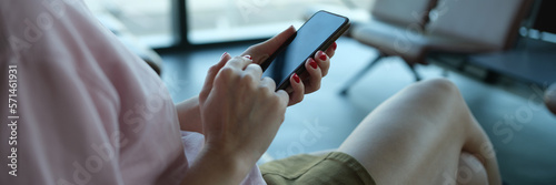 Woman traveler with smartphone in her hands sits in departure area at airport or train station