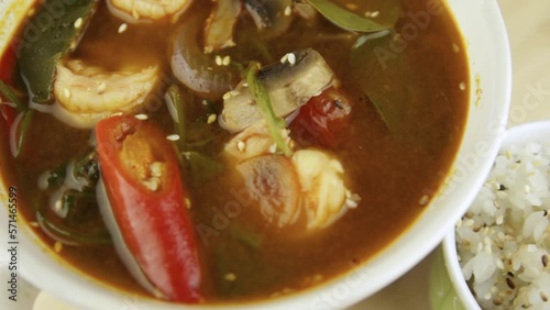 A bowl of tom yum soup. Shrimp, mushrooms, chili peppers. Rice in a small bowl.