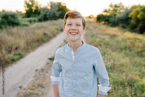 Portrait of smiling teenager boy standing in field in nature. Natural facial expression