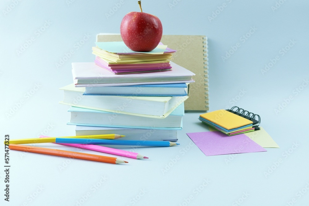 A stack of textbooks, colorful pencils, a sketchbook and a red apple, schoolboy education desk concept, back to school A stack of textbooks, colorful pencils, a sketchbook and a red apple, schoolboy education desk concept, back to school