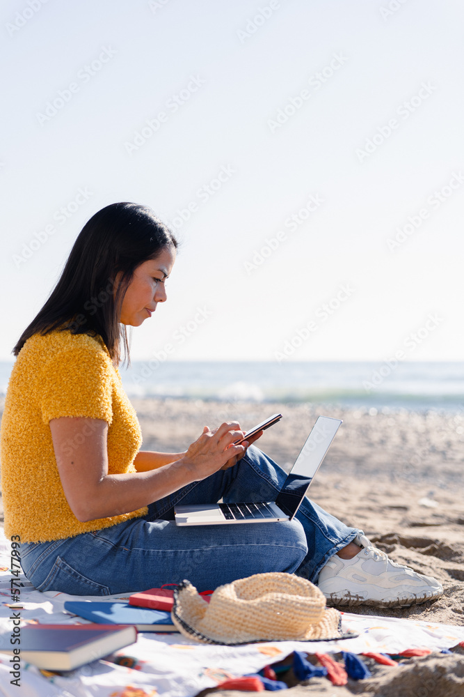 Taking notes in the agenda of the phone on a relaxing day at the beach of a Latin business woman in Spain. 