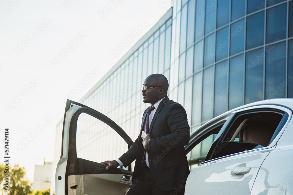 Portrait of a handsome successful African American businessman in a suit near his luxury car
