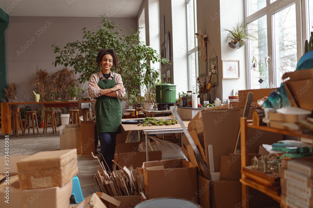 Attractive smiling florist stands with crossed arms on background of her own floral decor studio Attractive smiling florist stands with crossed arms on background of her own floral decor studio
