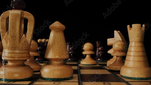 Chess game. A wooden chess pieces on a chess board in lights and shadows. Black background.