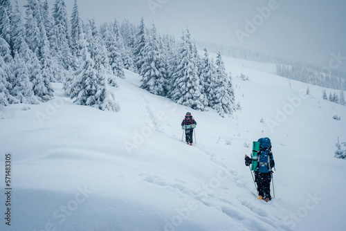 Hikers with backpacks make their way through snowy slopes on a frosty day.