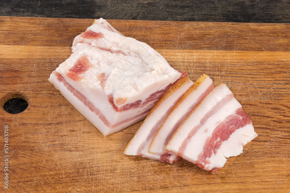 Partly sliced salted pork fatback on cutting board, close-up