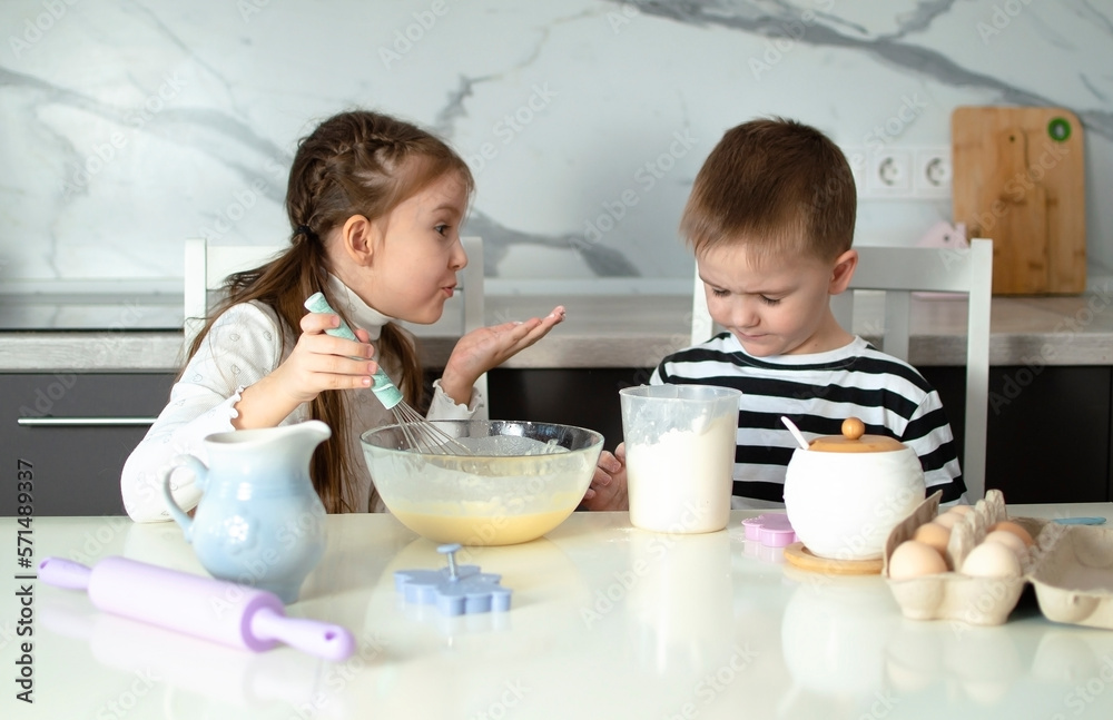Cheerful children bake cookies in white kitchen. Little girl likes to cook in kitchen. Happy child cooks dough, bakes cookies in kitchen. Children learn new things. Concept of children's leisure Cheerful children bake cookies in white kitchen. Little girl likes to cook in kitchen. Happy child cooks dough, bakes cookies in kitchen. Children learn new things. Concept of children's leisure