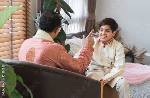 Indian handsome teenage son and father with traditional clothing sitting on sofa talking having conversation  smiling spending time together at home. Different aged generation communication in family