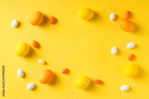 Yellow easter eggs with colorful candies on yellow background. Blank copy space on center.