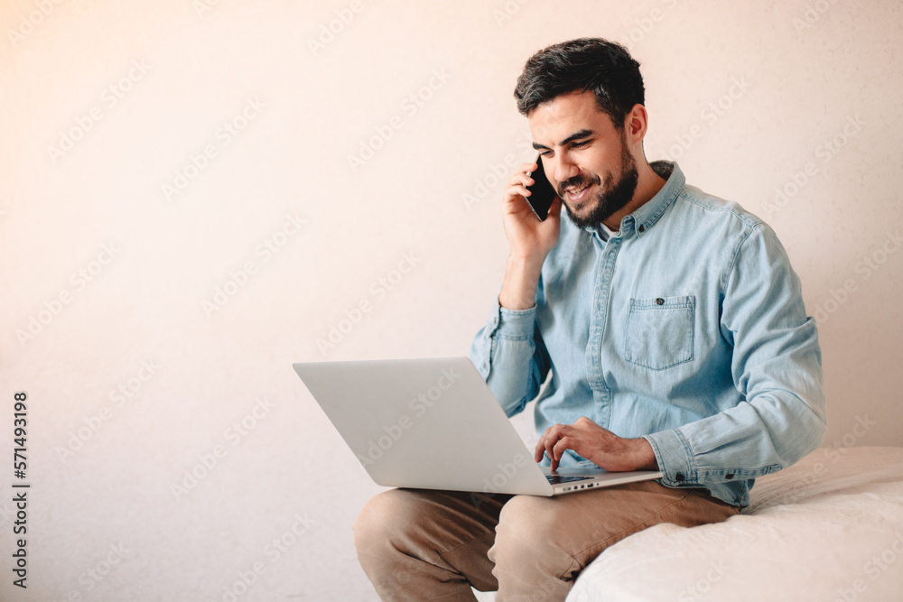 Happy businessman talking on smart phone while using laptop at home