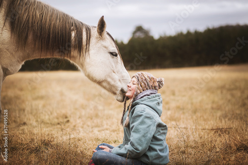 white horse tugging on girls hat in field in the fall while girl sits photo