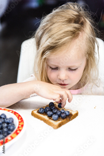 A little cute girl is eating her breakfast toast with blueberries photo