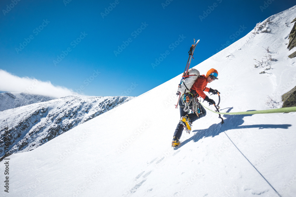 Man walking uphill with ice climbing tools and skis on his back Man walking uphill with ice climbing tools and skis on his back