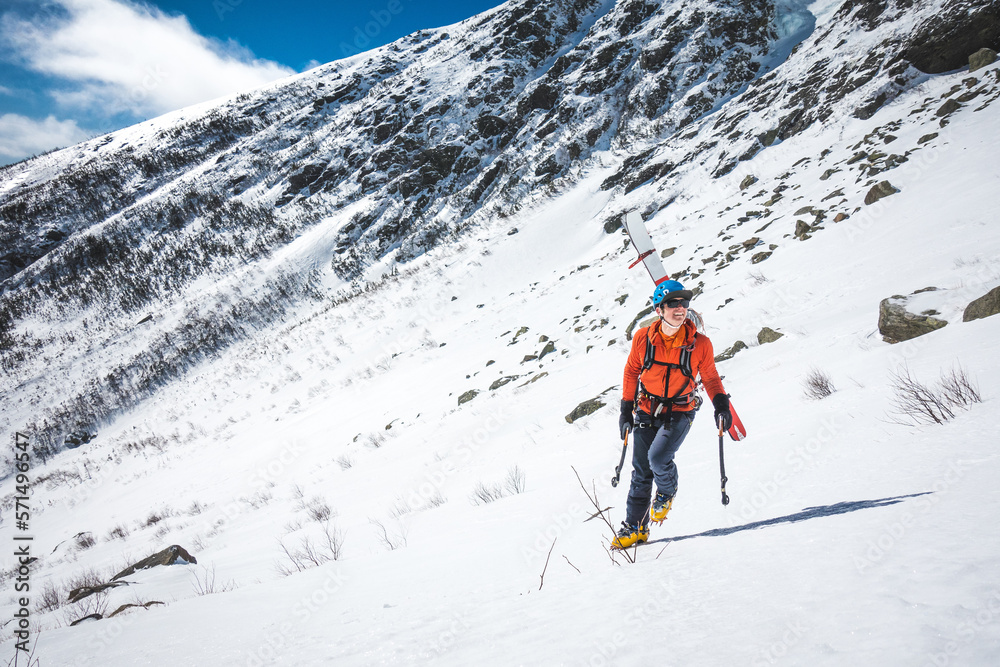 Man walking uphill with ice climbing tools and skis on his back Man walking uphill with ice climbing tools and skis on his back
