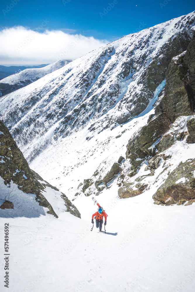 Man walking uphill with ice climbing tools and skis on his back Man walking uphill with ice climbing tools and skis on his back