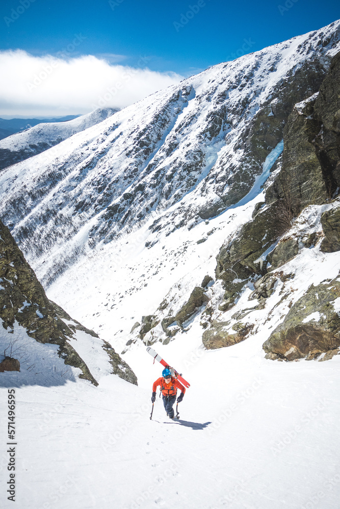 Man walking uphill with ice climbing tools and skis on his back Man walking uphill with ice climbing tools and skis on his back