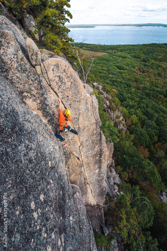 Woman rock climbing on vertical crack with ocean in background Woman rock climbing on vertical crack with ocean in background